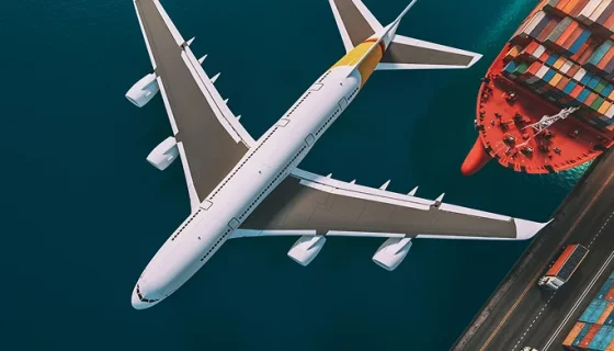 A white cargo aircraft on a runway being loaded with freight containers for delivery to Kuwait.